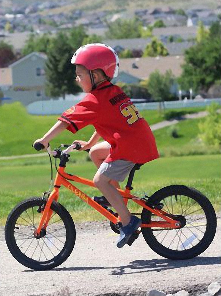 Jongen rijdt op een oranje kinderfiets zonder zijwieltjes over een grindpad