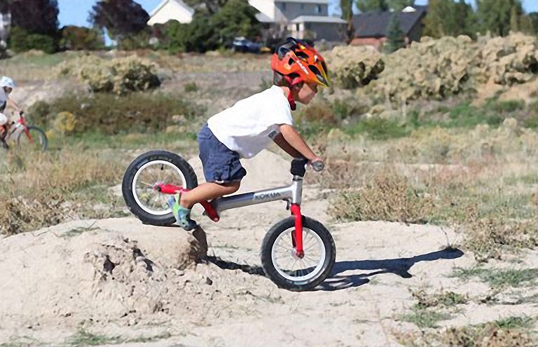 Jongen rijdt op een Kokua loopfiets over hobbelig, zanderig terrein