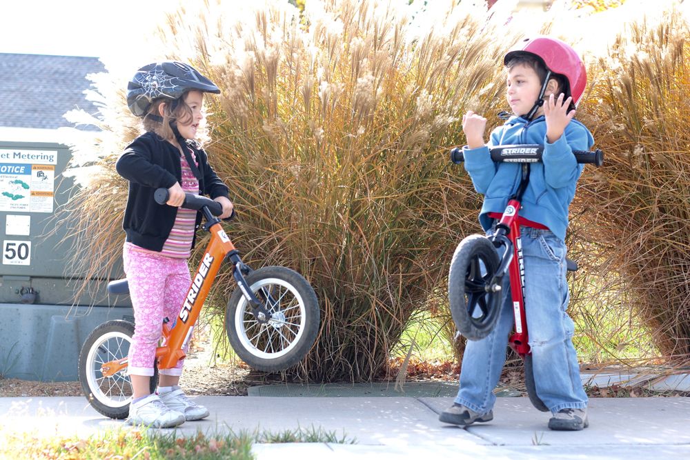 Twee kinderen met Strider loopfietsen; de jongen tilt zijn loopfiets moeiteloos met één hand op