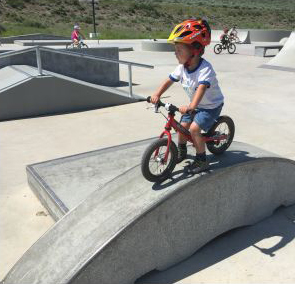Jongen rijdt zelfverzekerd met zijn loopfiets over een gebogen skate-obstakel