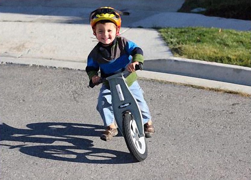 Lachende jongen rijdt op een grijze loopfiets over straat